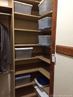 Plastic storage bins stacked on wooden shelves inside closet, bins are translucent with white lids.