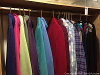Seventeen assorted women's jackets and shirts on hangers including fleece jackets and flannel shirts in various colors like purple, light green, turquoise, blue, red, and multi-colored patterns.