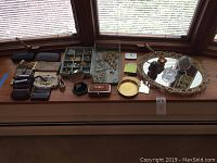 Full view of assorted bedroom decor, jewelry boxes, jewelry, and accessories laid out on a surface near a window.