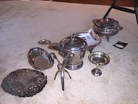 Overview of assorted silver and silver plated serving ware items arranged on carpet showing ice bucket, candy dish, candle holder, trays, small dishes, and electric casserole dish.