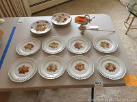 Set of 16 china desert plates with autumnal fruit designs, brass candle snuffer, and silver-plate sugar scuttle on table