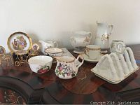 Overview of various bone china items including decorative plates, creamers, cup and saucer, and toast rack on a wooden surface.