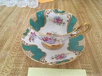 Fine bone china cup and saucer with turquoise and gold floral pattern displayed on wooden surface.