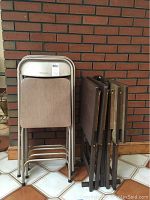Photo showing four beige padded metal folding chairs stacked against a brick wall.