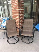 Two brown swivel patio chairs with metal frames and fabric seats placed outside next to a brick wall.