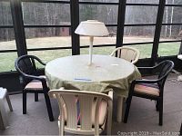 Full view of round outdoor table covered with fabric tablecloth with four plastic chairs around it, two black and two beige, all equipped with cushions.