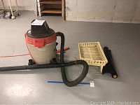 Ridgid wet dry vacuum with hose, extensions, and cream painted iron firewood grate and black tarp in basement