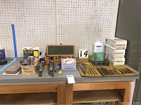 Overview of multiple assorted files, hand tools, stencils, and boxed parts arranged on a wooden table against pegboard.