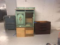 Front view of the antique armoire dresser painted green with floral details, showing open cabinet doors and separate drawers stacked on the side.
