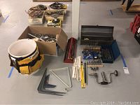 Overview of tool belt, boxes with hardware, metal brackets, set squares, manual hand drill, and assorted drill bits