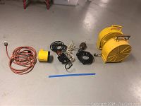 Electrical cords, yellow cord reels, flashlight, and hanging utility lights arranged on basement floor.