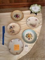 Six china plates arranged on a tablecloth; varied floral designs and edges, some with gold details, visible condition good.