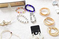 Overhead photo of various beaded bracelets in multiple colors and sets of gold-tone hoop earrings along with silver-tone dangling earrings on a soft surface