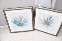 Two 11x11 framed abstract floral prints leaning against a wall, showing blue, gold, and gray brushstroke petals on white background.