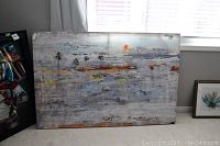 Front view of large abstract canvas wall art leaning against wall near window.