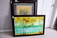 Two framed prints stacked with the botanical print of grass behind the landscape print with yellow-green trees and water