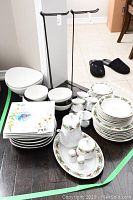 Wide view of the full lot showing stacked plates, bowls, and serving pieces organized on hardwood floor.