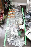 Photo of entire glassware assortment including dessert trays, multiple styles of wine and beer glasses, clear mugs, and additional glass items on a green-bordered tray.