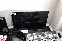 Front view of LG TV with screen off, placed on floor under window, lot sticker 805 visible