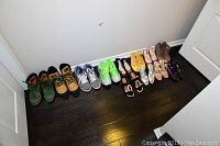Full view of all shoes arranged in a single row on dark hardwood floor against a white wall, showing a variety of styles and colors.