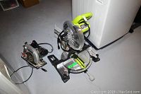 Photo shows Ryobi miter saw with green handle and Skilsaw circular saw on floor near washing machine.