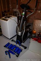 Wide angle photo showing the Tempo Fitness elliptical stepper, adjacent to a washing machine and an AB Rocket abdominal machine in foreground.