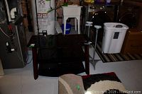 Front view of 3 tier black glass and wood TV unit with visible wear, and two metal and wooden speaker stands beside it.