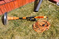 Side view of the Orange and black Electric Worx corded weed trimmer lying on grass with attached cutting head guard and loop handle.