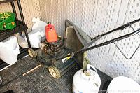 Full view of a black gas-powered lawn mower with red fuel tank, beige wheels, and grass catcher bag inside a storage area.