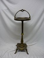 Front view of the Art Deco ash-stand showing round tray top, curved handle, and tripod base.