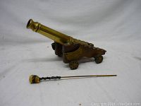 Full view of brass miniature cannon on wooden carriage with tamping rod positioned in front