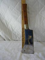 Full length photo of the meat cleaver next to a ruler showing approximately 15.5 inch length. Wooden handle with three rivets and metal blade with wear and markings.