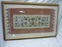 Front view of framed vintage embroidered fabric with floral and abstract multicolored patterns on pink backing in gold frame.