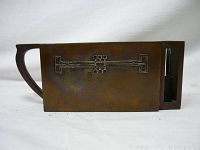 Side view of the rectangular copper holder showing geometric linear decoration and handle.