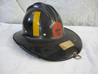Front and side view of a vintage black fibreglass fireman's helmet with yellow stripe and red emblem.