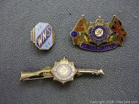 Three WWII-era sterling silver pins displayed on fabric: WNS pin, Canadian Army Service flag pin with motto, and rifle-shaped pin with emblem.