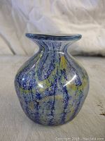 Front view of the small hand-blown glass vase showing the blue and yellow swirl decoration on the rounded body and flared rim.