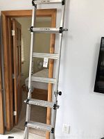 Full view of the aluminum extendable ladder leaning against a wall indoors, showing the upper section and locking knobs.