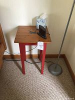 Pine wood table with natural finished rectangular top and red painted legs, placed against wall on carpeted floor beside a standing lamp and tissue box on top.