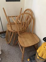 Set of six natural wood chairs stacked, showing curved spindle backs and flat seats.