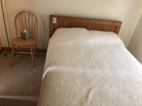 Full view of pine wood bed frame and headboard with chair next to it for scale, mattress included for representation only.
