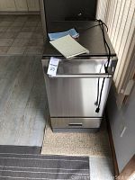 Front view of the stainless steel ice maker showing handle, control panel, power cord draped over top, and notebook placed on unit