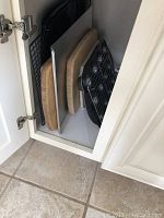 Metal cookie sheets, wooden cutting boards, and black metal rack arranged vertically inside a cabinet