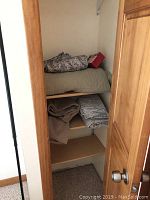Closet shelf containing folded quilt with floral pattern, and folded bed linens in brown and gray tones.