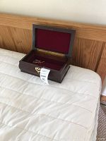 Open wooden jewelry box placed on a white quilted surface, showing red lined interior and brass latch.