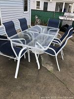 Full view of patio set, table and chairs on concrete surface with gas grill in background