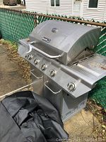 Front and side view of NEXGRILL gas BBQ grill showing four burner control knobs plus one for the side burner and the built-in temperature gauge on the lid. Grill shows signs of use.
