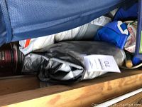Photo of a large gray tarp folded with a white label within a storage area alongside other items