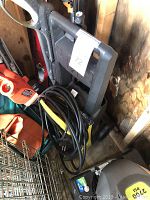 Yellow and black Karcher pressure washer unit in storage with cord wrapped and attached.