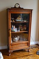 Full front view of the oak-finish cabinet with three shelves and decorative feet